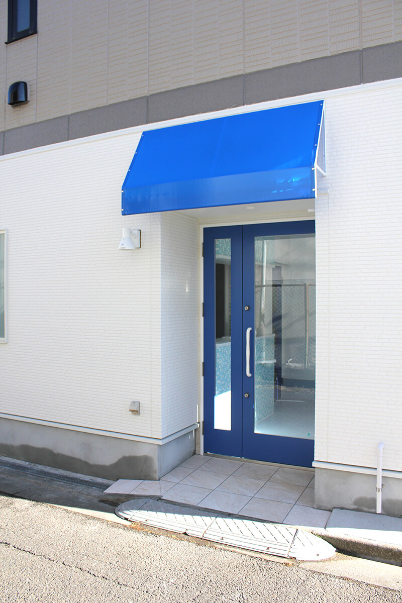 調布市のほほえみ動物病院は、佐須街道から路地に入ってすぐのところに病院の入り口があります。青い屋根と扉が目印です。